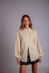 Camisa de manga larga con diseño abullonado, confeccionada en tela bordada con motivos florales. Presenta cierre frontal con botones y puños elásticos.