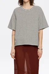 Camiseta de punto roma con rayas horizontales blancas y negras, corte recto y manga corta ancha. Presenta un escote redondo y un detalle de nervio vertical en el centro delantero.