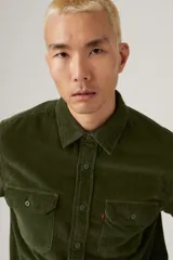 Camisa de pana color verde militar, con cuello clásico, cierre de botones frontales y dos bolsillos con solapa en el pecho.