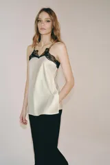 Top de tejido satinado color crema con escote en pico y tirantes finos. Presenta detalles de encaje negro en contraste en el escote y bajo recto.