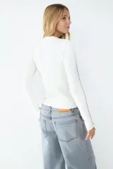 Sweater de manga larga color crudo, confeccionado en tejido de canalé elasticado. Diseño ajustado con cuello redondo y costuras decorativas en contraste color rosado en el frente, la espalda y las mangas.