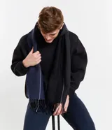 Bufanda unisex de lana acrílica con textura sargada y flecos en los extremos. Diseño bicolor: un lado azul marino con una fina línea blanca y otro lado negro con una fina línea blanca.