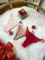 Pack de tres tangas de encaje con diseño floral, breteles regulables y laterales finos. El conjunto incluye una tanga rosa claro, una tanga color tostado con bordes grises y una tanga roja.
