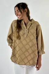 Blusa beige con cuello mao, escote en V con volados y cierre de botones. Presenta mangas 3/4 con puños elásticos y diseño con textura de rombos.