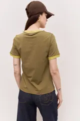 Remera estilo ringer de manga corta, color verde militar, con cuello y puños en contraste amarillo. Presenta una estampa gráfica frontal de inspiración surf con la frase "Team Brava".