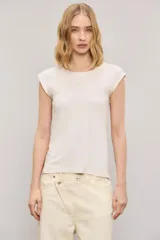 Remera color blanco roto, de calce slim, cuello redondo y manga corta con detalle de hombreras y pequeño bordado en el centro del pecho.
