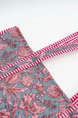 Bolso tipo tote bag de tela acolchada con estampado floral en tonos gris y blanco. Presenta asas largas reforzadas con detalle de rayas en los bordes.