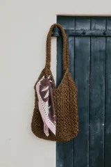 Bolso tipo shopper de tejido de paja o rafia en color crudo, con textura calada y asas cortas integradas al cuerpo del bolso.