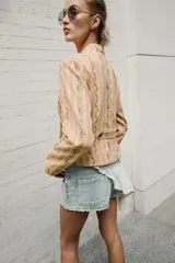 Cazadora de jacquard con estampado de rayas y detalles florales en tonos rosados y beige, cuello redondo, manga larga, bolsillos delanteros de vivo y cierre frontal cruzado con botones metálicos.