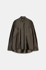 Camisa de corte holgado confeccionada en mezcla de lyocell con acabado satinado. Presenta cuello redondo con lazadas integradas, cierre frontal con botones ocultos bajo solapa, bolsillos de plastrón en el frente y mangas largas con puños anchos. El bajo es asimétrico y redondeado.