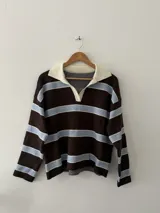Sweater de punto con diseño a rayas horizontales en tonos marrón, celeste y blanco. Presenta cuello polo con solapas en color crema, manga larga y corte holgado.