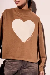 Sweater marrón de algodón peinado con cuello alto y calce oversize. Estampado frontal de corazón blanco con texto en cursiva.