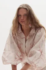 Vestido largo de lino con estampado floreado en tonos rosados, cuello camisero, botonadura frontal de nácar y mangas amplias abullonadas con puños elásticos. Presenta aberturas laterales en la falda.