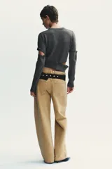 Jersey de punto gris oscuro, cuello redondo y manga larga. Presenta detalles desmontables con botones a lo largo de las costuras de las mangas y en el ruedo inferior.