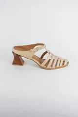 Sandalias de cuero color beige estilo cangrejera con punta fina, diseño de tiras entrelazadas, tira ajustable en el tobillo con hebilla dorada y taco geométrico de madera.