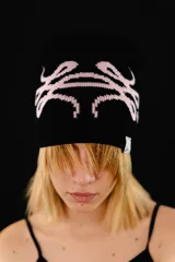 Beanie tejido reversible, con un lado negro y el otro lado rosado claro, ambos con diseño gráfico estampado en contraste.