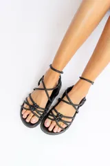 Sandalias bajas negras de cuero con tiras tubulares entrecruzadas y pulsera tobillera.