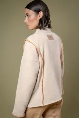 Buzo de lana color beige con cuello redondo y costuras decorativas bordadas en color naranja a lo largo de los laterales y puños. Presenta un diseño holgado y mangas largas.
