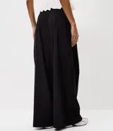 Pantalón de sastrería negro de cintura alta, con pinzas frontales y diseño fluido de perneras anchas.