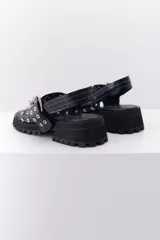 Sandalia de cuero color marrón con suela track negra. Presenta dos tiras frontales con ojalillos metálicos y una tira trasera con cierre de velcro.