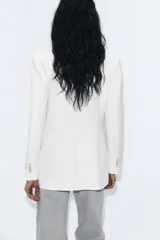 Blazer blanco de manga larga con cuello solapa y hombreras. Diseño cruzado con cierre frontal de cuatro botones y bolsillos delanteros con solapa.