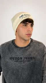 Gorro tipo beanie de punto color crema con bordado gráfico en la parte frontal.