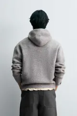Chaqueta de punto con capucha, corte relajado, manga larga, bolsillos laterales y cierre frontal con cremallera. Presenta acabados en rib en puños y bajo.