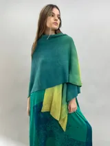 Ruana de lana merino con diseño en degradé de tonos verdes. Presenta un cuello plisado artesanalmente en fieltro de lana merino, ofreciendo una textura suave y un acabado elegante.