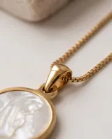 Collar de acero con baño de oro y cadena fina de eslabones, con un dije circular dorado que presenta una imagen en relieve de la Virgen sobre fondo de nácar.
