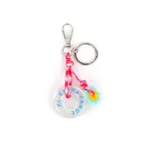 Llavero con mosquetón y argolla metálica, compuesto por un cordón de tela estampado en tonos rosados, un dije circular transparente con la inscripción 'Extra Large' en azul y un dije pequeño en forma de flor celeste con centro amarillo.