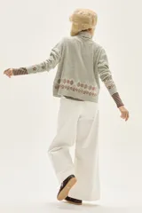 Polera de tejido de punto en color gris, con cuello alto y diseño holgado. Presenta un aplique central en color crema con motivos ornamentales y detalles bordados geométricos en la parte inferior y en las mangas.