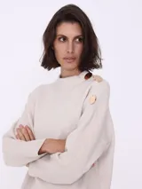 Sweater color beige de tejido de punto, con cuello redondo y mangas largas. Detalle de botones dorados en el hombro.