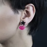 Par de aros colgantes con forma de labios rosados con glitter y corazón plateado con glitter.