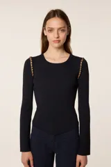 Sweater de punto fino color negro, con cuello redondo y mangas largas. Presenta un diseño ajustado con un corte asimétrico en el ruedo delantero y detalles de cuentas doradas en las costuras de los hombros.