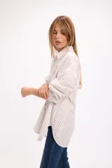 Camisa de corte oversize con estampado de rayas verticales finas en color marrón sobre fondo blanco. Presenta cuello clásico, cierre frontal con botones, bolsillo en el pecho y mangas largas con puños abotonados.
