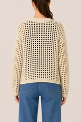 Buzo de punto en color beige, con diseño de trama abierta tipo red, cuello redondo y terminaciones acanaladas en puños y ruedo.