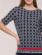 Remera de algodón con estampado geométrico en blanco y negro, de manga corta, con detalle de guarda roja y flecos en el ruedo.