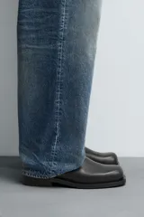 Bota de piel negra con diseño minimalista, cierre de cremallera lateral, horma cuadrada y suela a tono con ligero tacón.