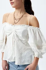 Top blanco con hombros descubiertos, bordado con detalles de puntilla y frunces en el frente. Tiene mangas abullonadas y breteles finos.