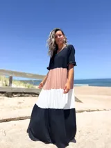 Vestido largo de diseño tricolor con bloques de color en negro, beige y crudo. Presenta escote en V, mangas cortas con volados y una falda amplia con cortes horizontales que crean un efecto escalonado.