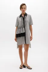 Vestido camisero a rayas verticales blancas y grises, con cuello clásico negro, cartera con volados y mangas cortas. Detalle de volado lateral con terminación irregular.