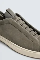 Zapatilla urbana de hombre confeccionada en piel con acabado de serraje, diseño minimalista con cordonera oculta y suela de goma a contraste.