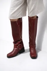 Botas de cuero croco color rojo oscuro, de caña alta (38 cm), con taco bajo de 3 cm y punta cuadrada. Presentan un arnés decorativo con hebilla metálica alrededor del tobillo.