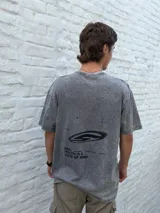 Remera gris oscuro con efecto acid wash, corte oversize y manga corta. Presenta un estampado minimalista en negro con texto que incluye "TRUTH IS A STATE OF MIND" y un logo gráfico.