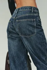 Jeans de mujer, tiro alto, color azul medio con efecto desgastado (lavado claro en muslos y oscuro en bordes). Corte recto y ancho (mom fit) con cinco bolsillos y cierre frontal de botón y cremallera.