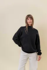 Sweater tejido de punto color blanco, con cuello alto y diseño en relieve tipo chevron en la parte frontal. Presenta un calce holgado con terminaciones acanaladas en puños y ruedo.