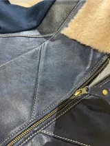 Campera con cuerpo de cuero sintético azul marino y mangas de lana tejida al tono. Presenta cuello solapa con forro de piel sintética en color beige, cierre frontal con cremallera y costuras decorativas visibles en el frente.