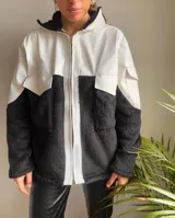 Campera negra y blanca con cierre frontal, parte superior de cuerina blanca, parte inferior de peluche negro y cuello alto con forro de peluche.