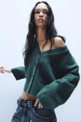 Chaqueta de punto de textura suave en color marrón oscuro, con escote en pico, manga larga y cierre frontal con botones. Presenta dos bolsillos de plastrón en la parte delantera.