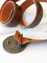 Cinto de cuero color marrón con forro de cuero y hebilla redonda con detalles de guampa. El broche es suizo, para poder usar el cuero con otras hebillas.